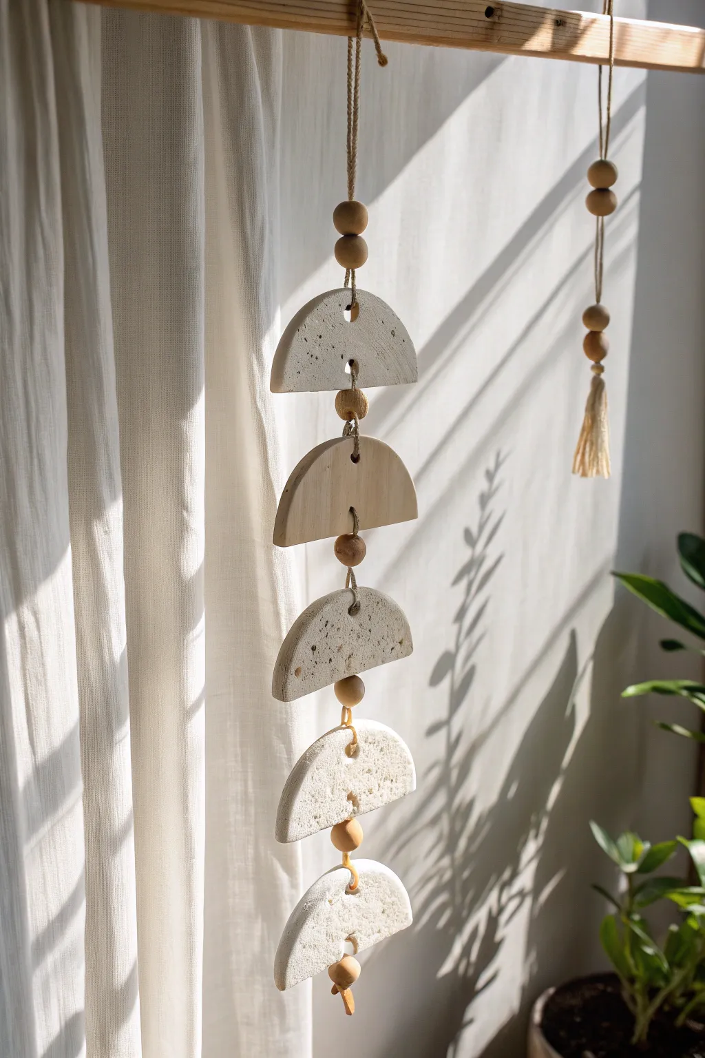 Minimal clay suncatcher with cutouts, glowing in a sunny window and casting soft shadows.