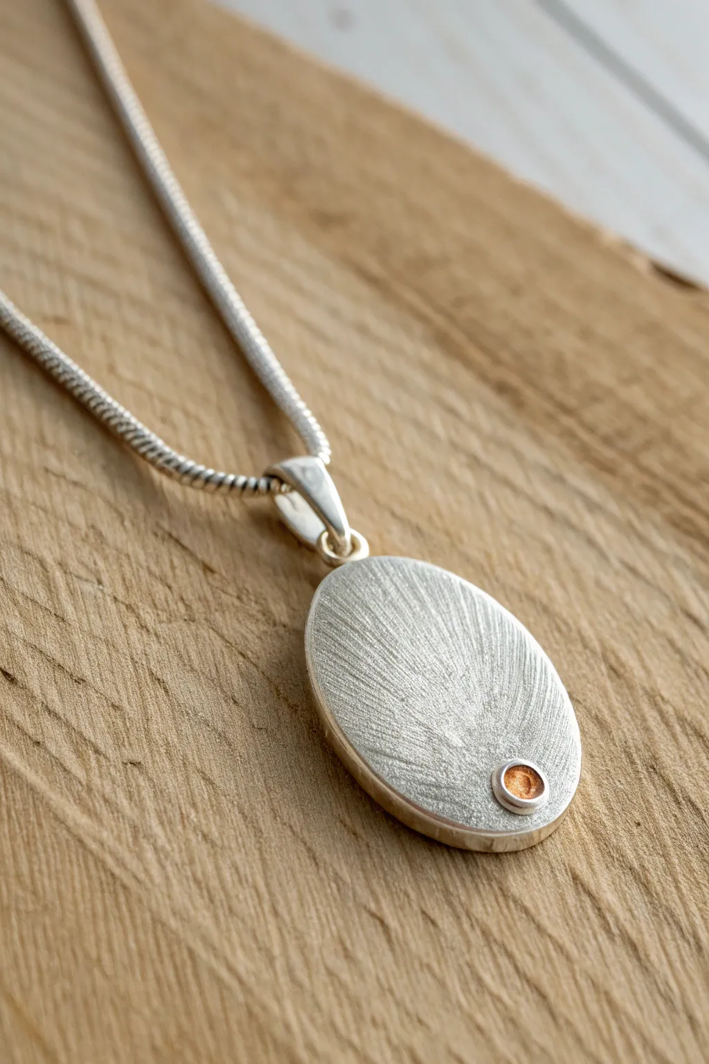 Two-tone surprise: matte silver clay pendant with tiny warm accents on a pale wood base.