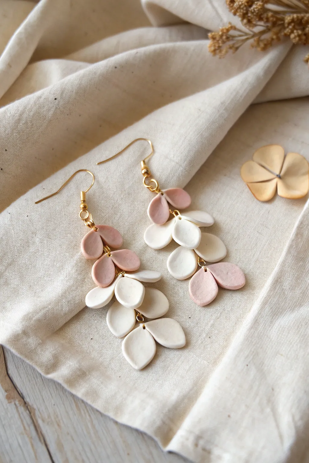 Sculptural air dry clay petal earrings with soft blush shading on natural linen, minimalist boho.