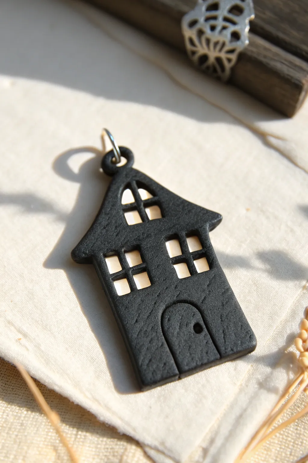 Minimal haunted house pendant in matte black clay, clean cutouts on a soft linen backdrop