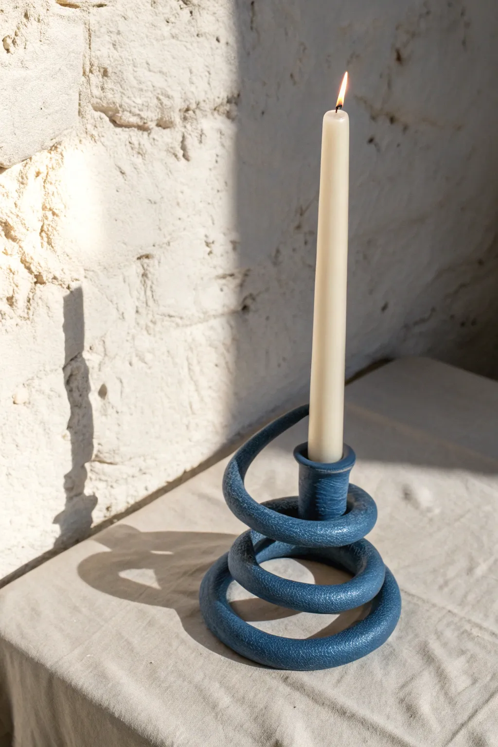Coiled clay snake candle holder in bold matte color, casting dramatic shadows in warm candlelight