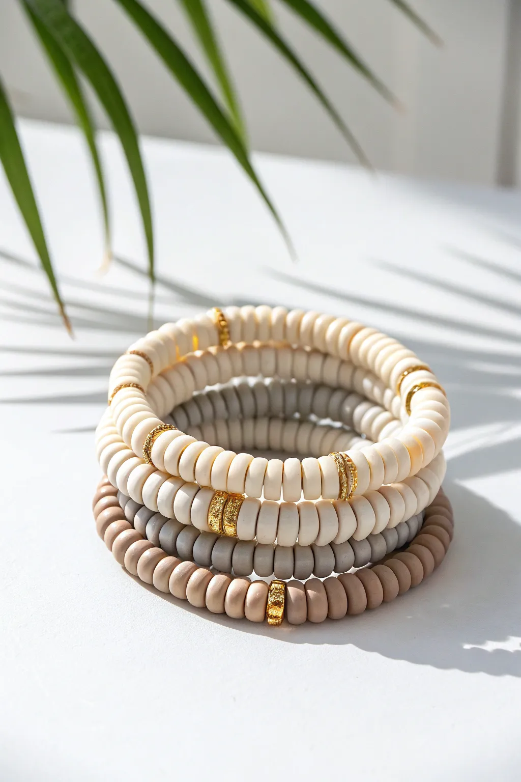 Clean neutral clay disc bracelets stacked with tiny gold spacers on a bright white backdrop.