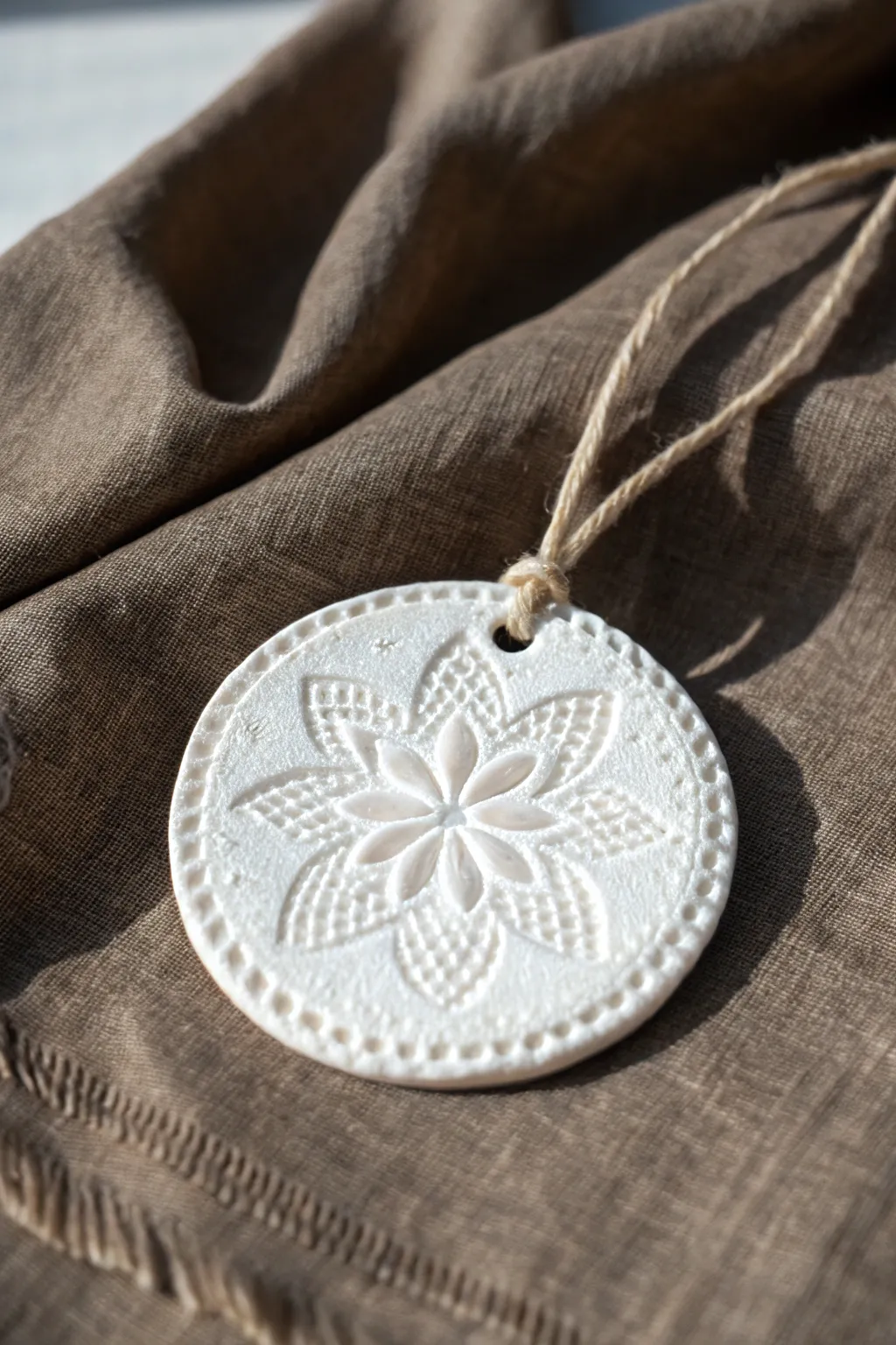 Matte white stamped clay medallion ornament with linen string, minimalist boho charm.