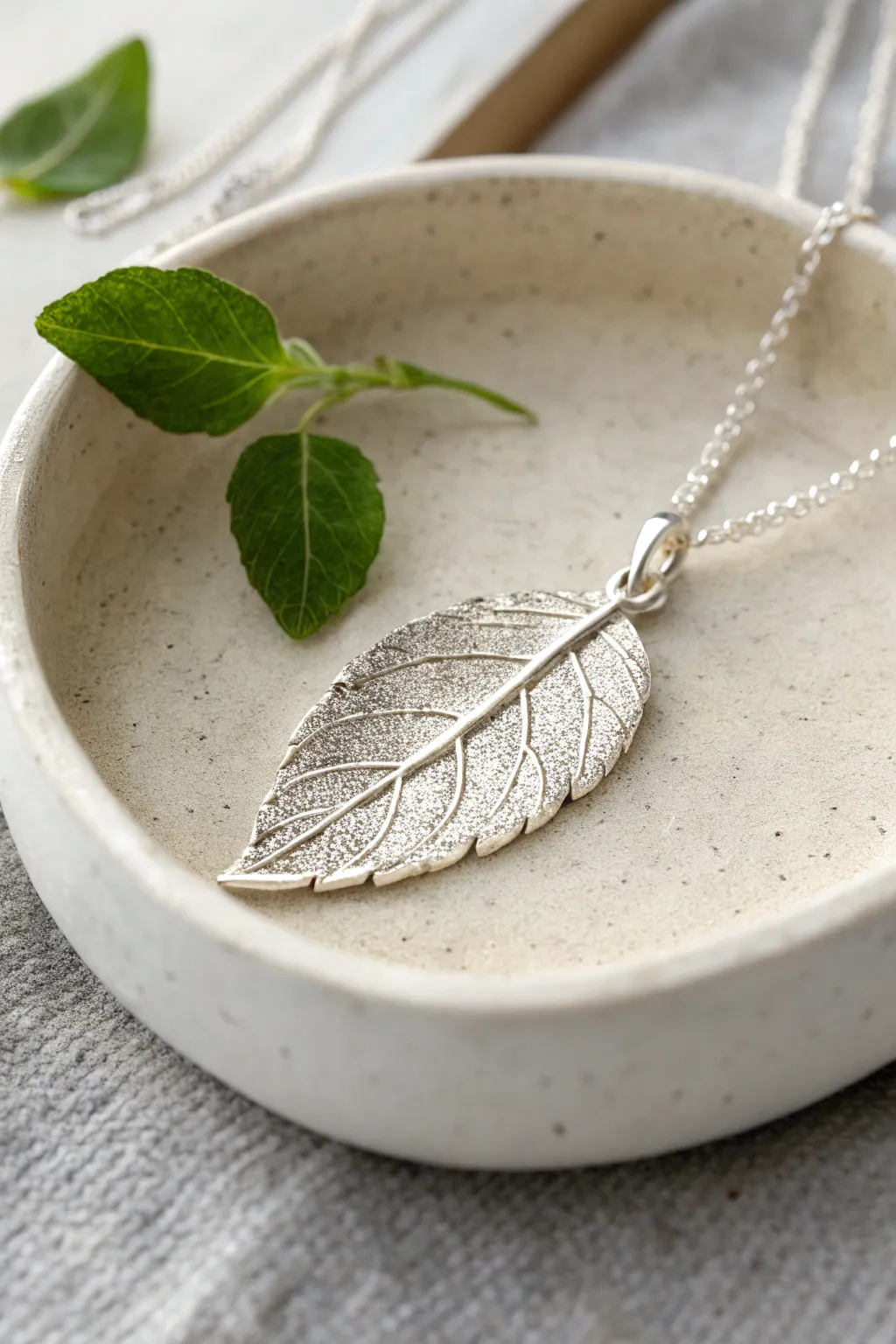 Leaf-imprint silver clay pendant with crisp veins, styled with a real leaf for natural elegance.