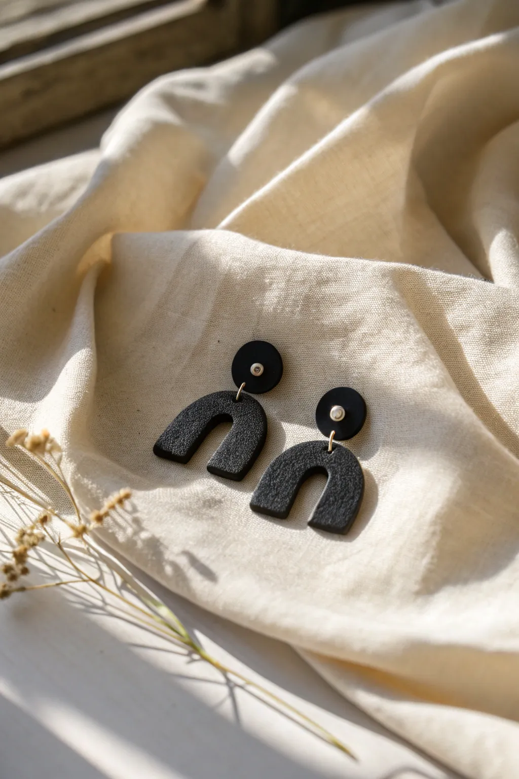 Minimalist black clay earrings with tiny white detail, styled on linen for a Scandi boho look.