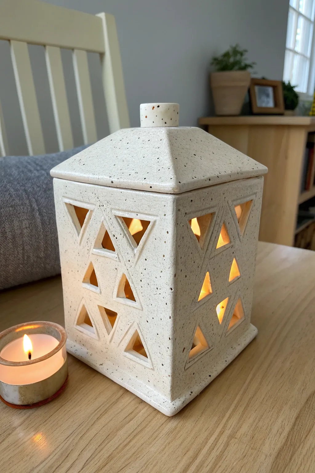 Minimal slab-built ceramic box lantern with geometric windows, glowing warmly on a tidy side table.