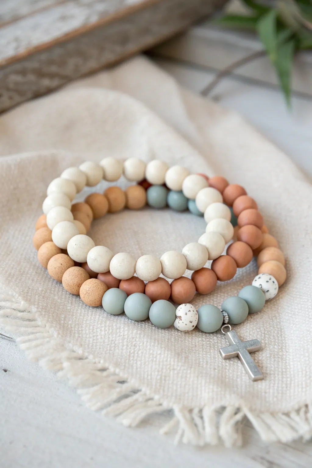 Minimal clay bead bracelet stack with a simple cross focal point in soft, neutral tones.