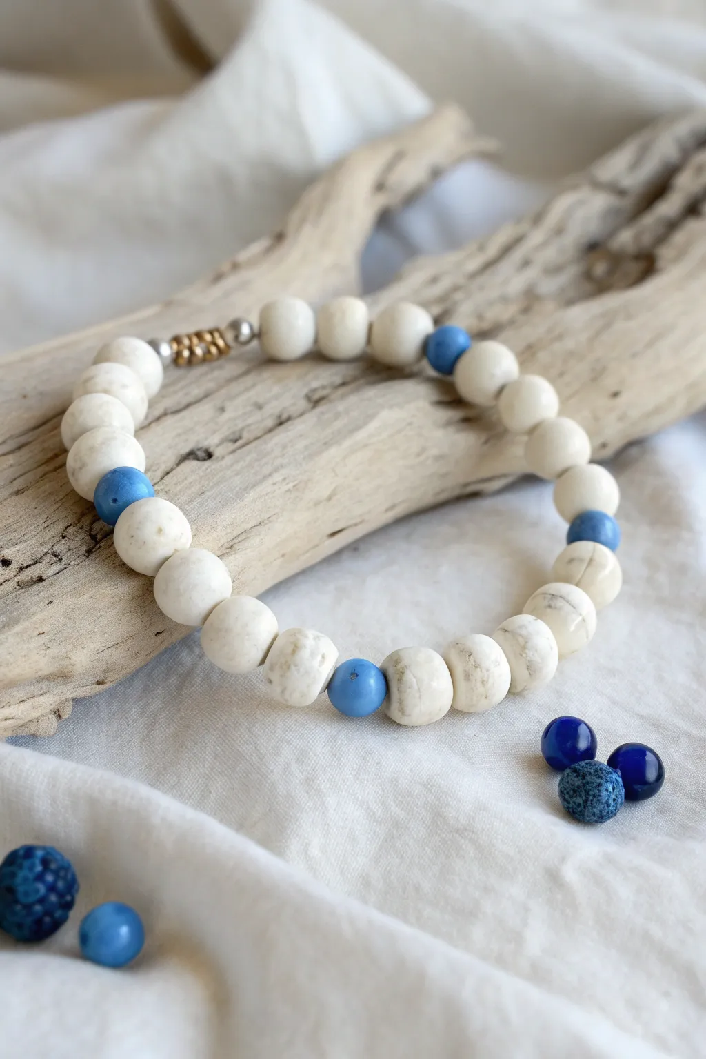 Wide white clay bead bracelet with tiny blue pops, styled on pale driftwood in minimalist boho mood