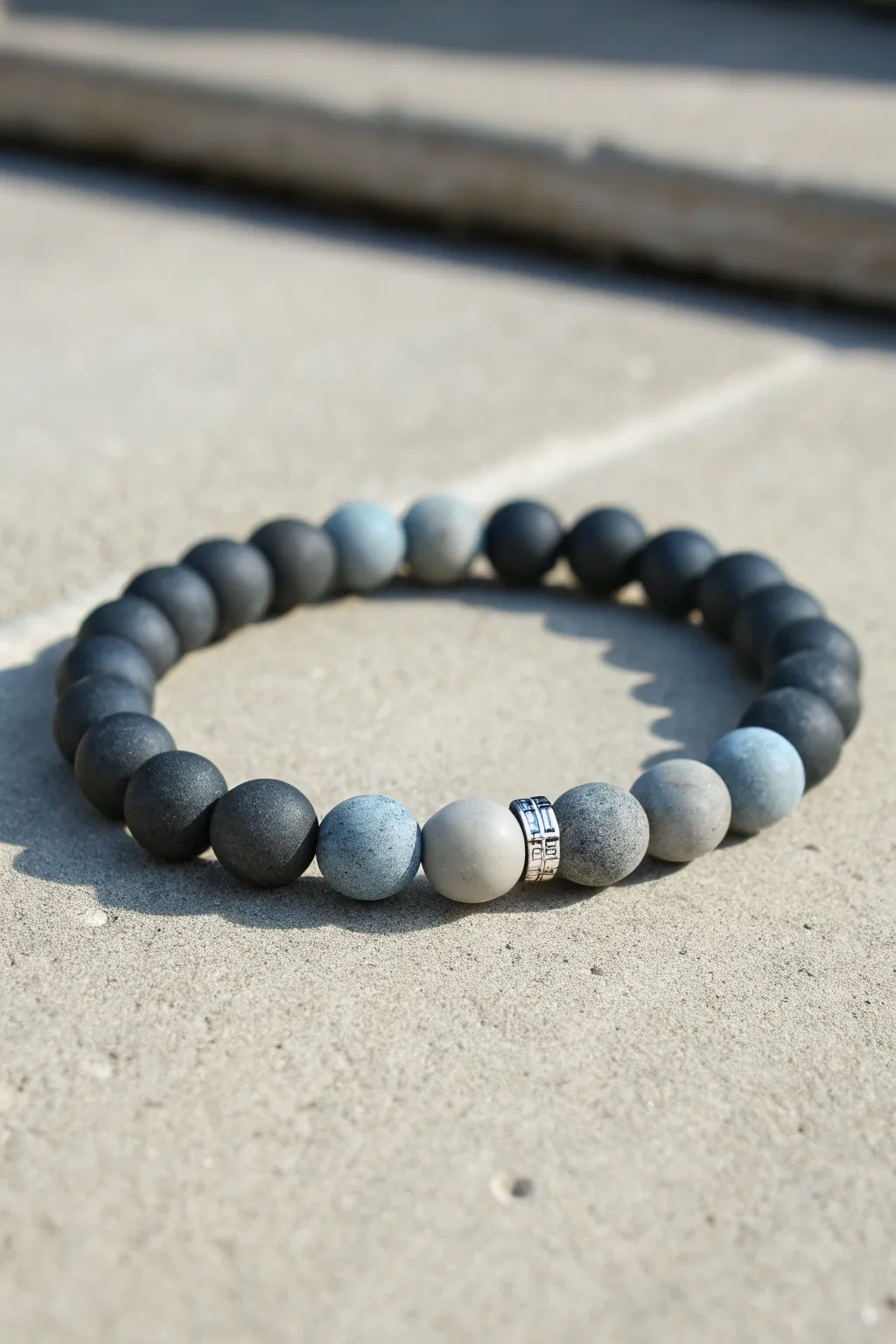 Charcoal-to-gray clay bead bracelet with clean gradient fade, minimalist and modern on concrete.