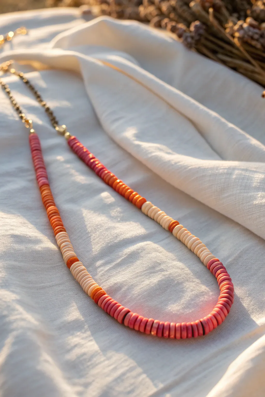 Sunset ombre clay heishi necklace in hot pink to peach, glowing on white linen
