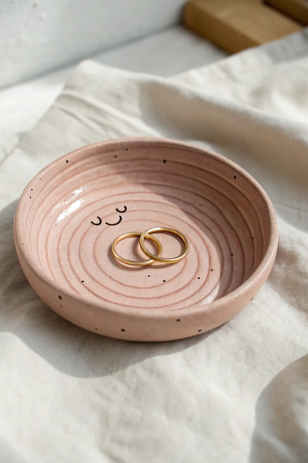 Simple coil ring dish with a sweet face, finished in soft blush clay and holding two rings.