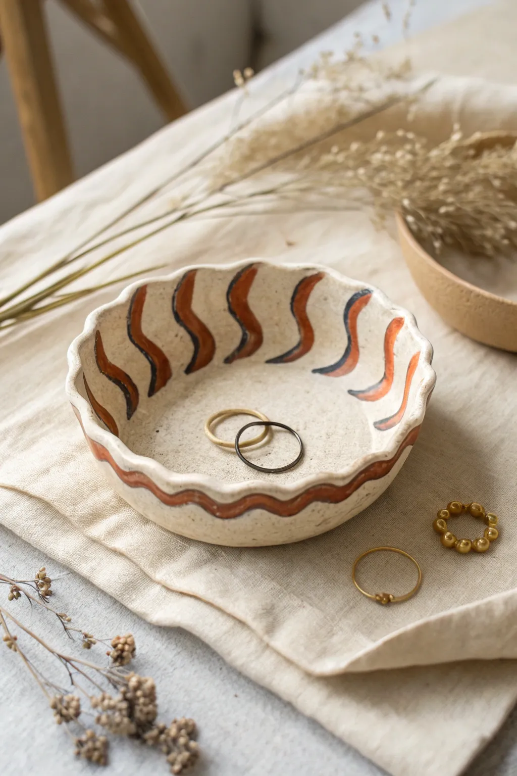 Wavy painted trinket bowl with bold stripes, holding rings and earrings in minimalist style.