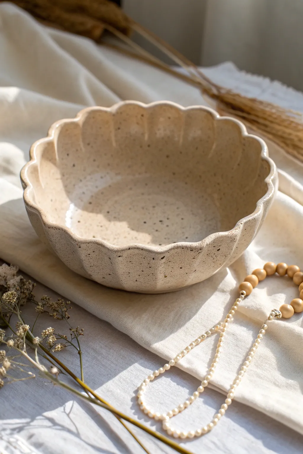 Scalloped pastel clay bowl with a flowerlike rim, styled with a dainty necklace on linen.
