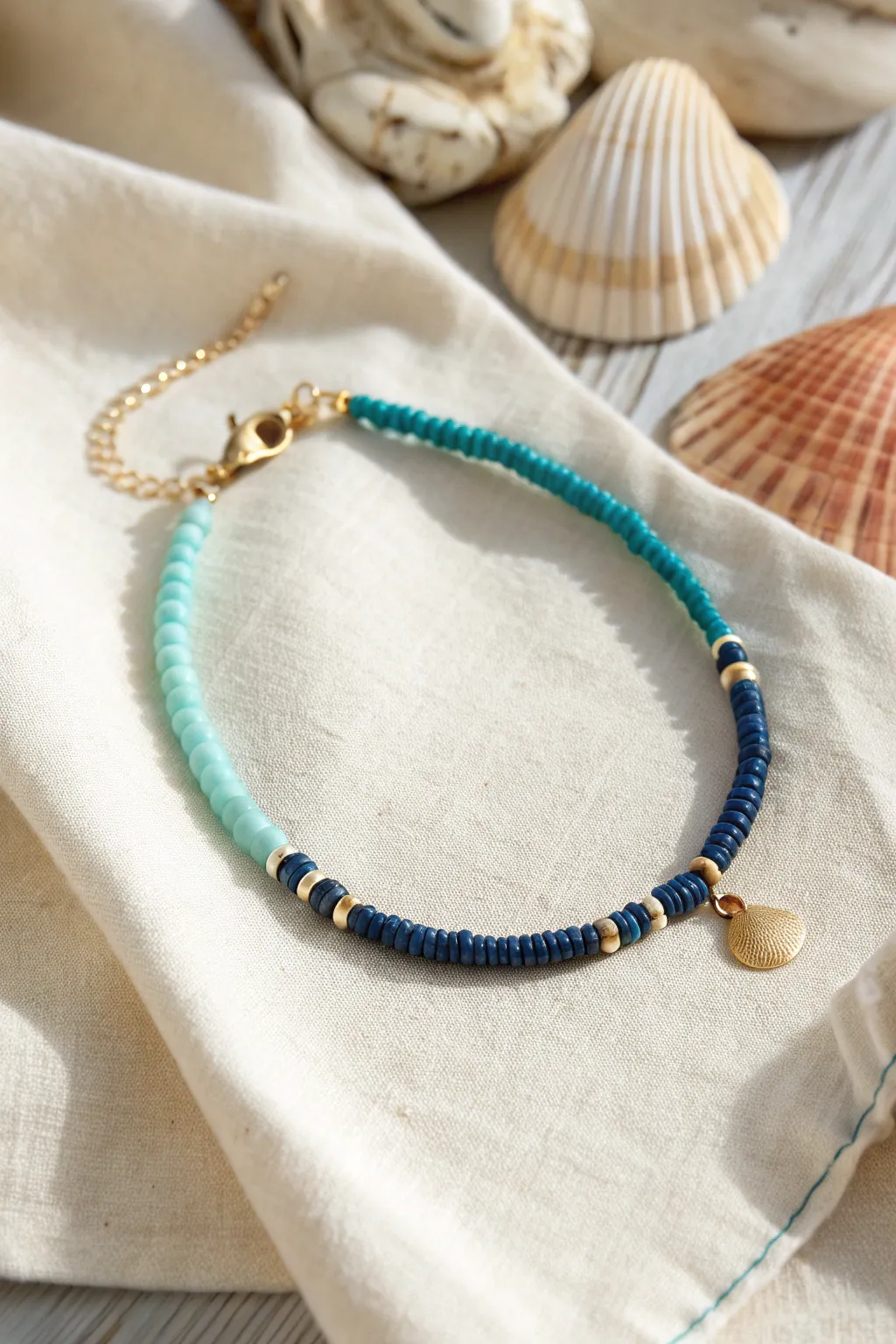 Ocean blues clay heishi bracelet in an aqua-to-navy gradient with a tiny shell charm