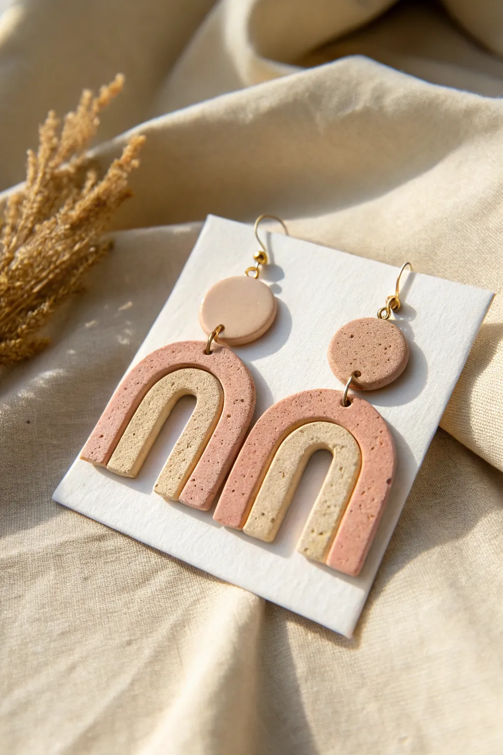 Minimal geometric polymer clay dangles in soft neutrals, styled with clean shadows and calm texture.