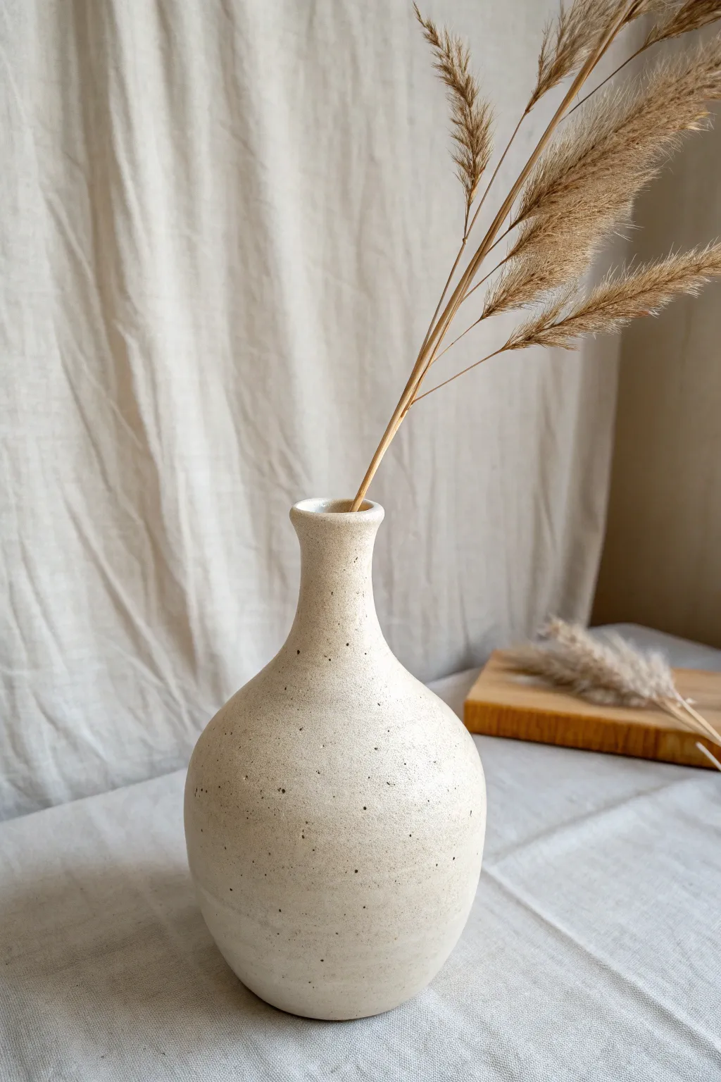 Narrow-neck pinch pot bottle vase with a single dried grass stem in calm minimalist styling.