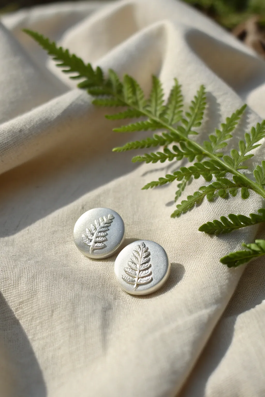 Delicate fern-textured silver clay stud earrings styled on linen for a soft, minimal look