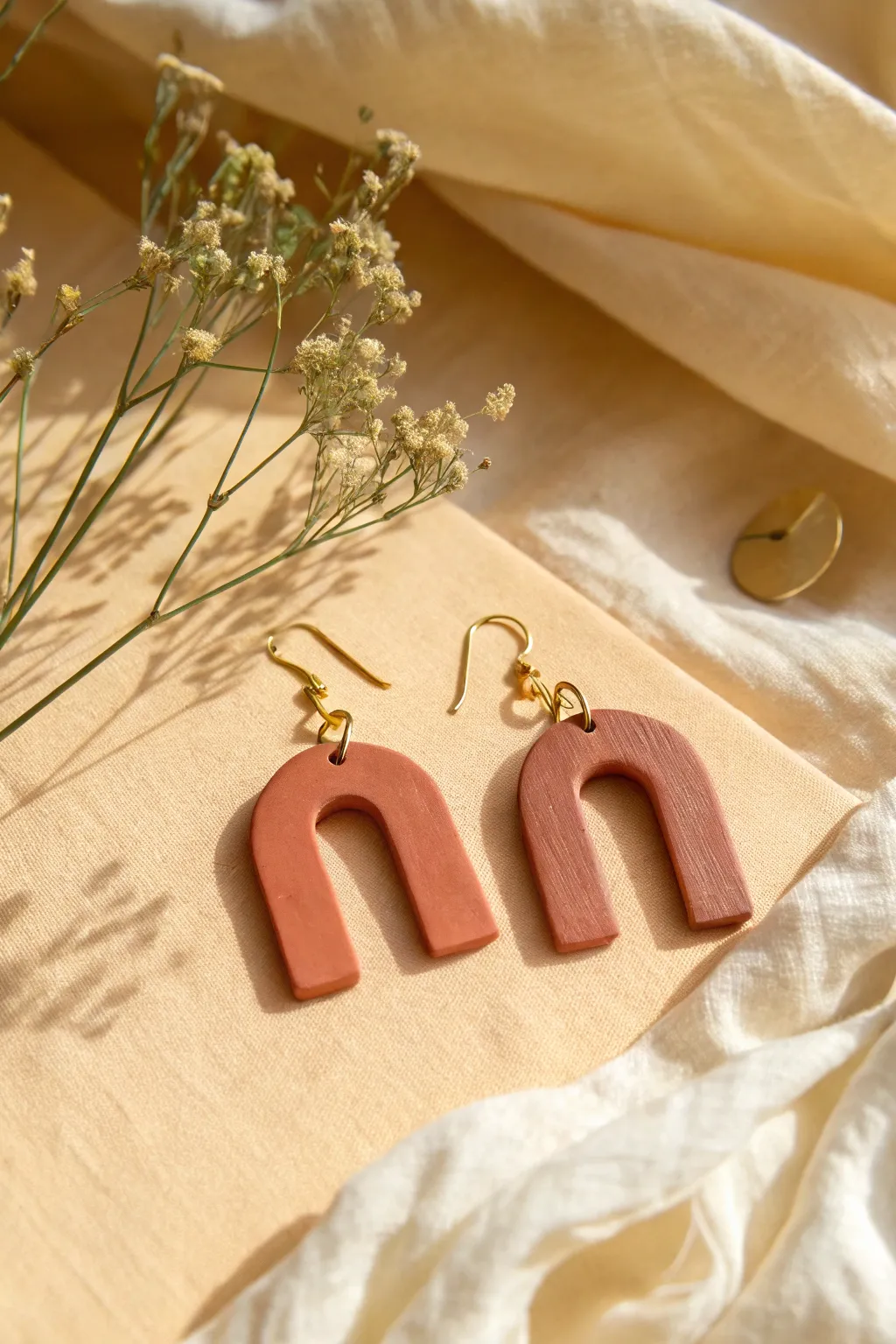 Minimal arch terracotta earrings in matte finish, styled on cream linen for warm Scandinavian calm.