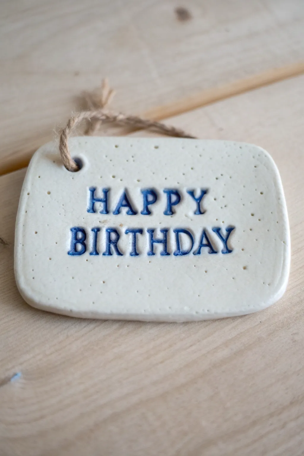 Handmade clay Happy Birthday plaque with bold raised letters and ribbon hole, minimalist gift-ready.