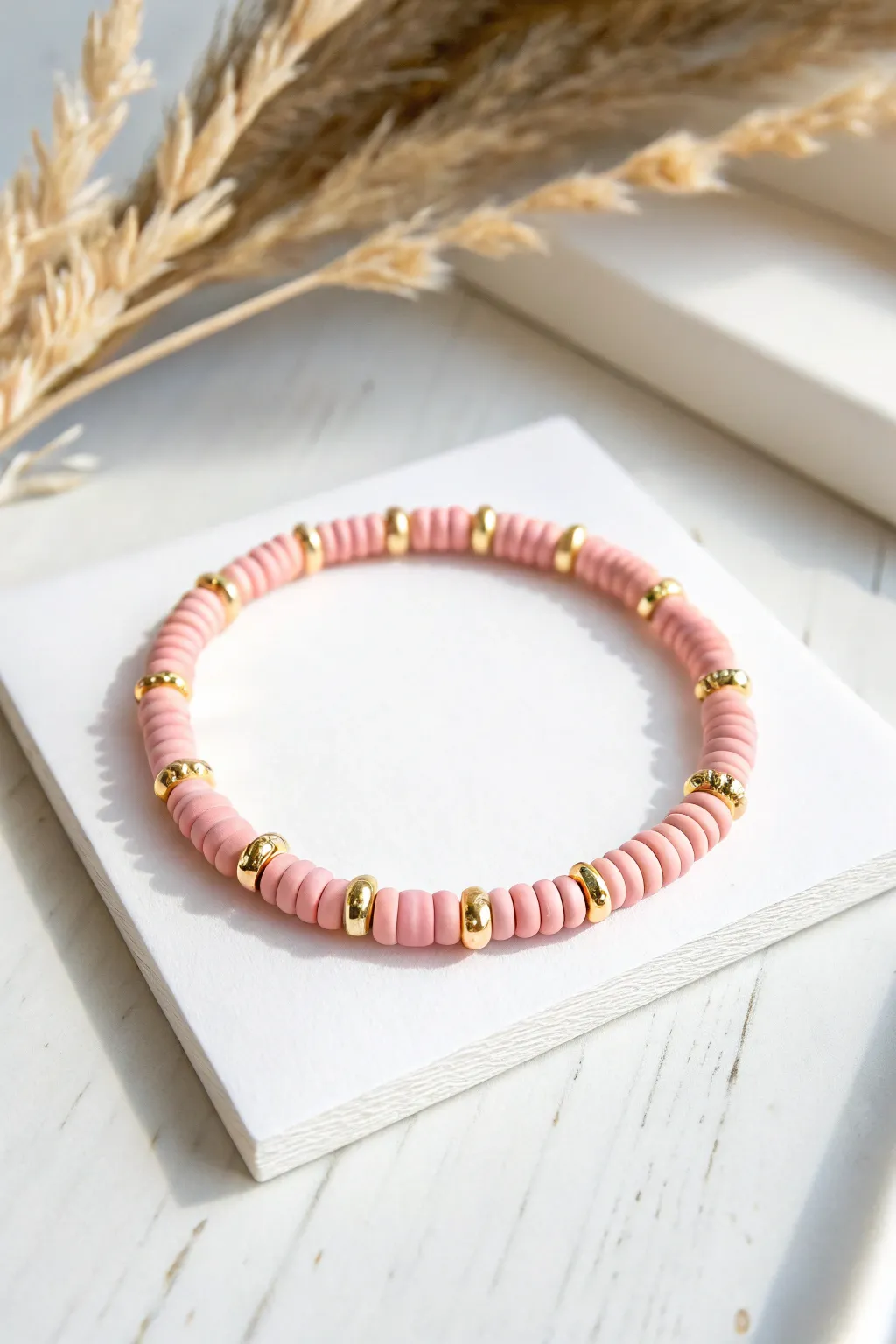 Blush pink heishi bracelet with gold spacer rhythm, minimalist flat lay on white cardstock.