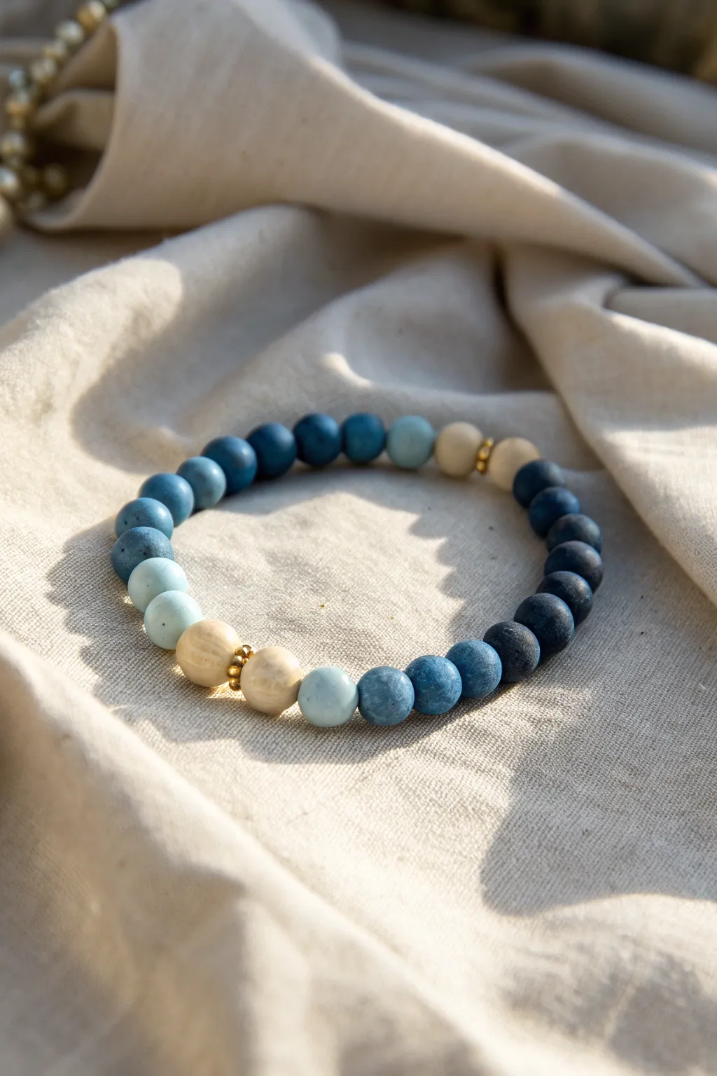 Monochrome clay bead bracelet in calming blue tones, styled simply on natural linen.