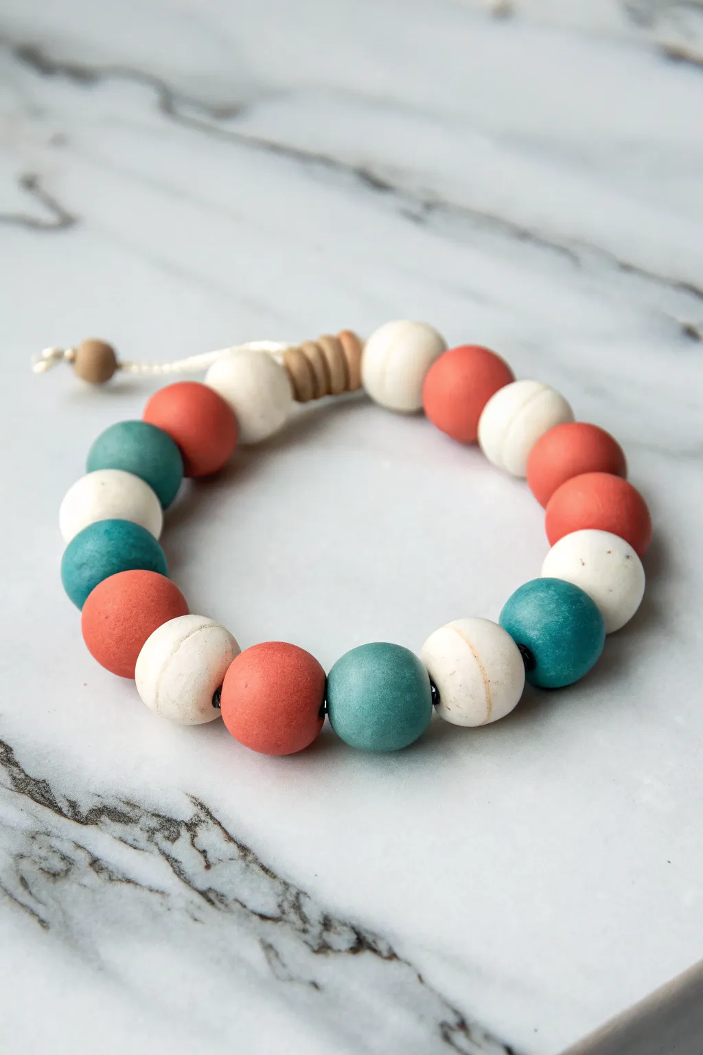 Bold color-block clay bead bracelet in white, coral, and teal on a clean marble backdrop