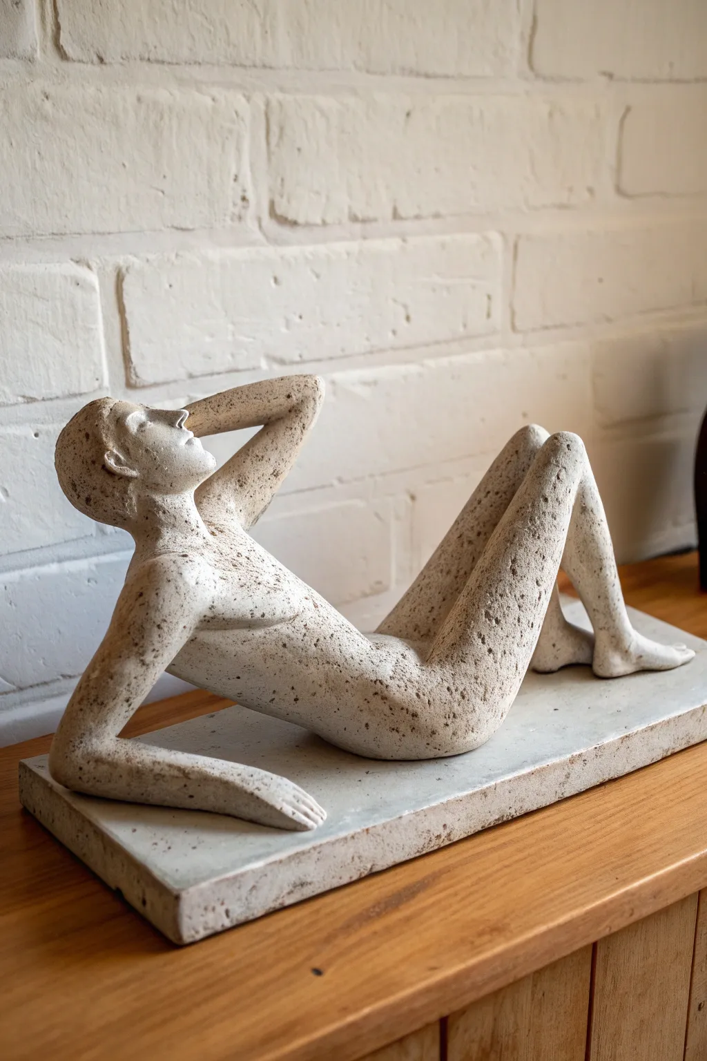 Reclining clay figure on a slim slab, calm curves and cozy shadows for minimalist charm.