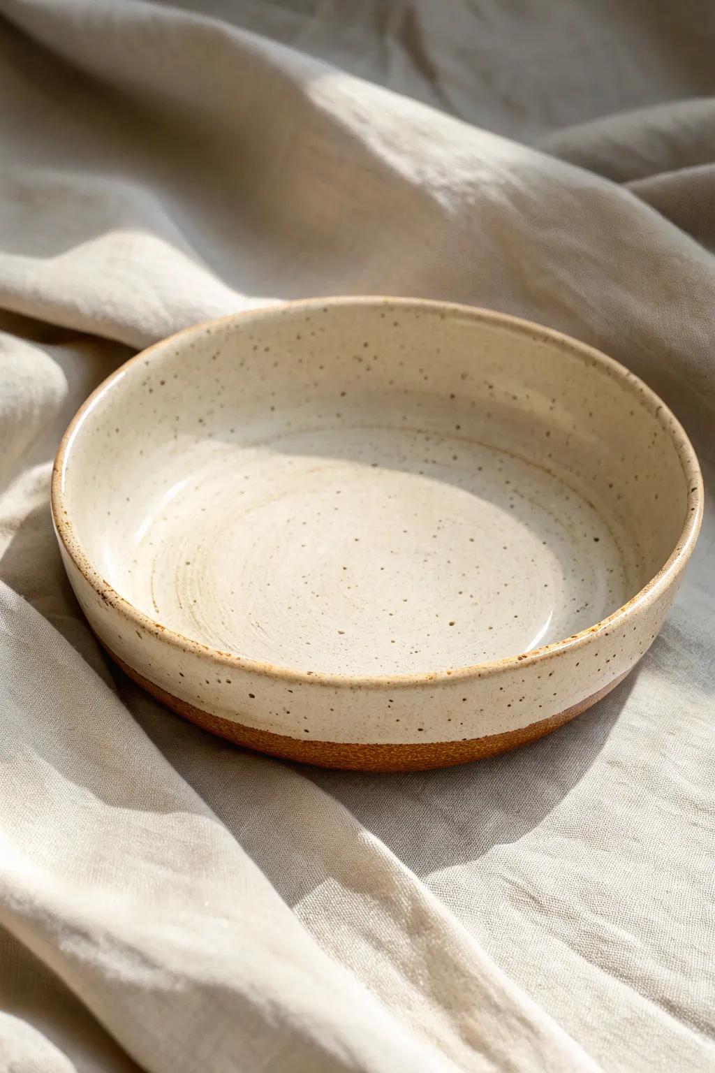 Simple slumped slab bowl with clean curves and soft speckled glaze, styled in calm neutrals.