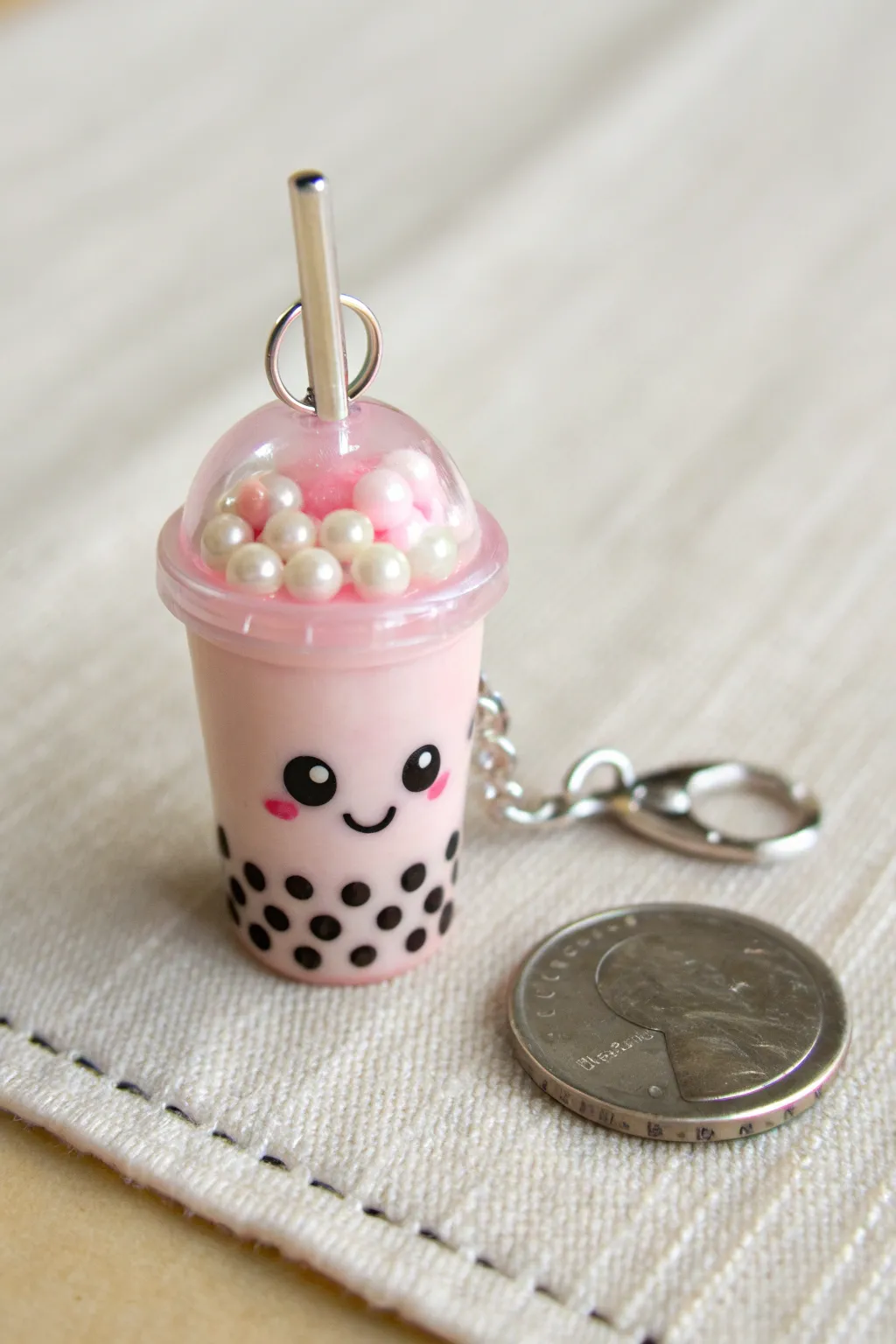 Pastel bubble tea charm with tiny pearls and a sleepy smile, photographed beside a coin for scale.