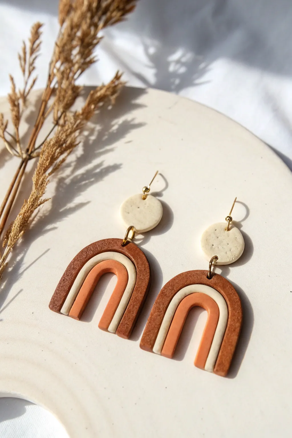 Modern polymer clay arch dangles in muted tones, Scandinavian minimal styling with soft shadows