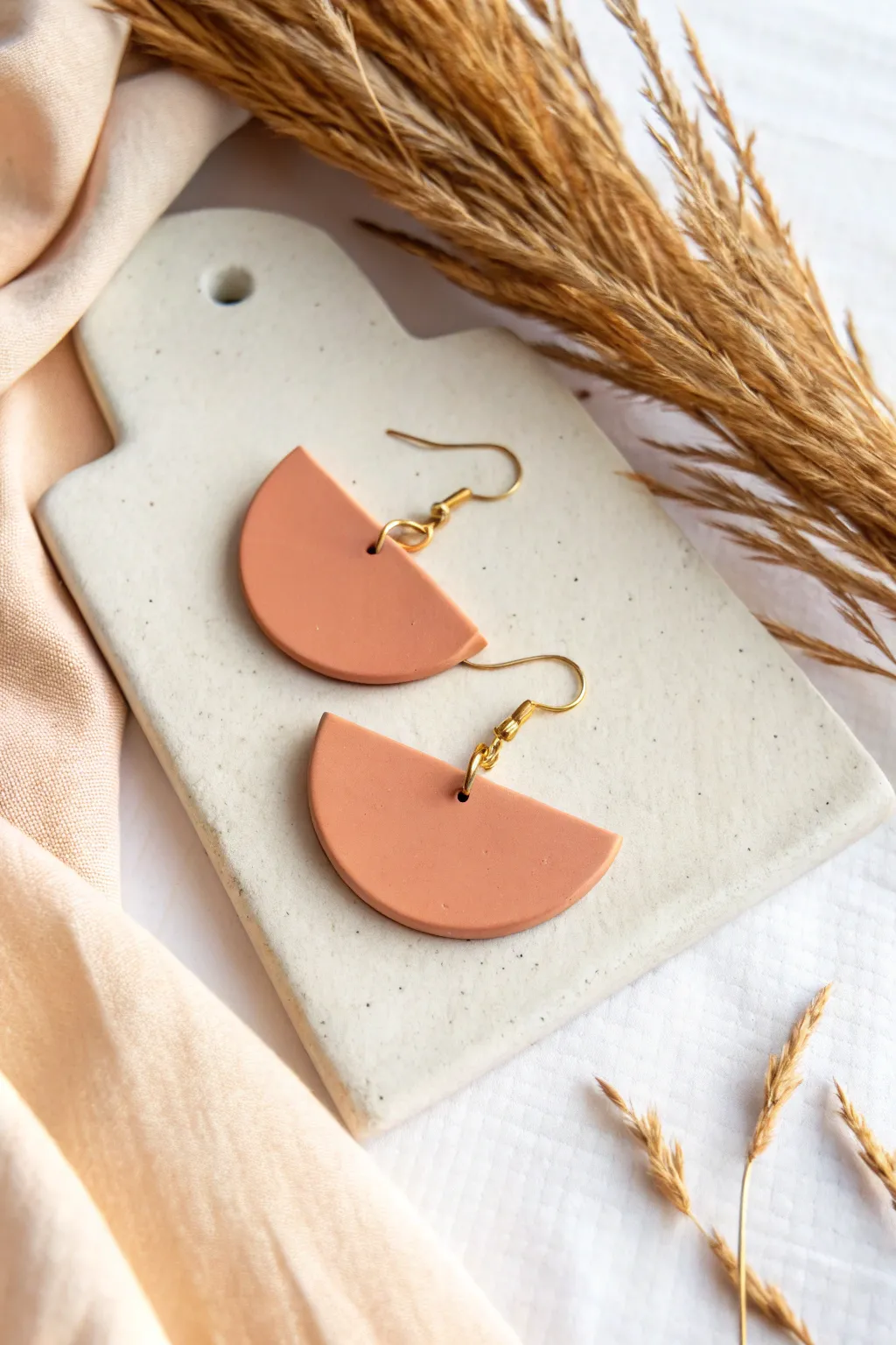 Half-moon clay earrings in soft blush with minimal gold hooks, bold yet airy for everyday wear.