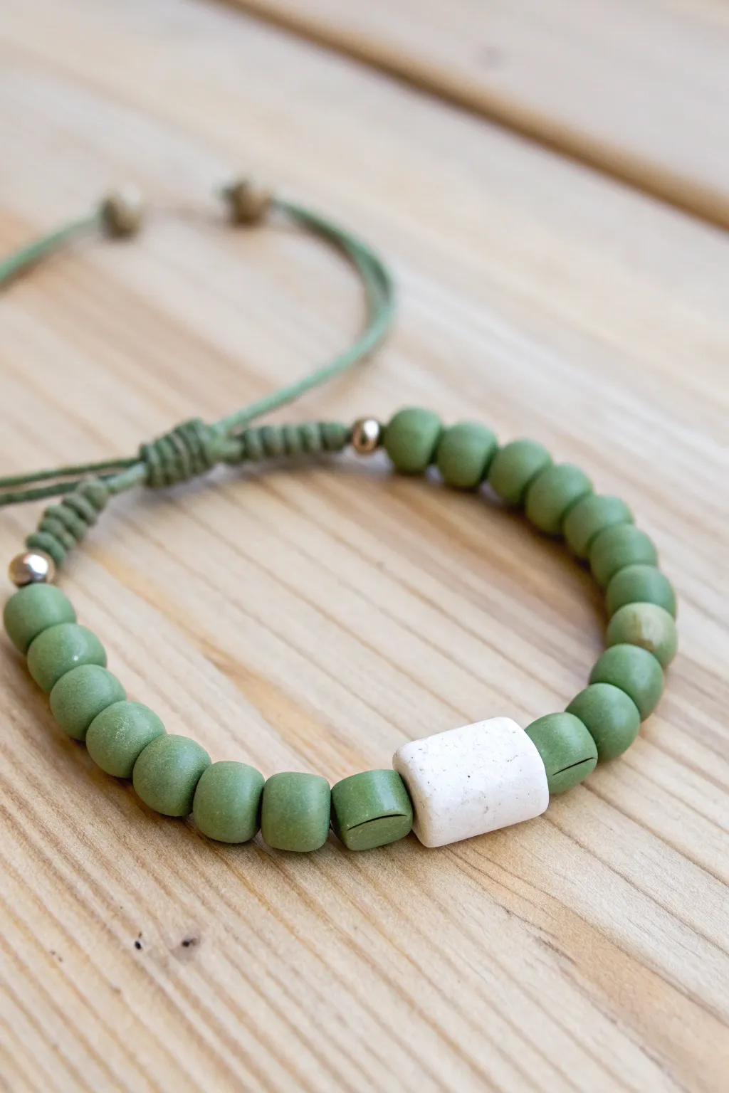 Clean color-block bracelet: sage green beads framing a crisp white center on pale wood.
