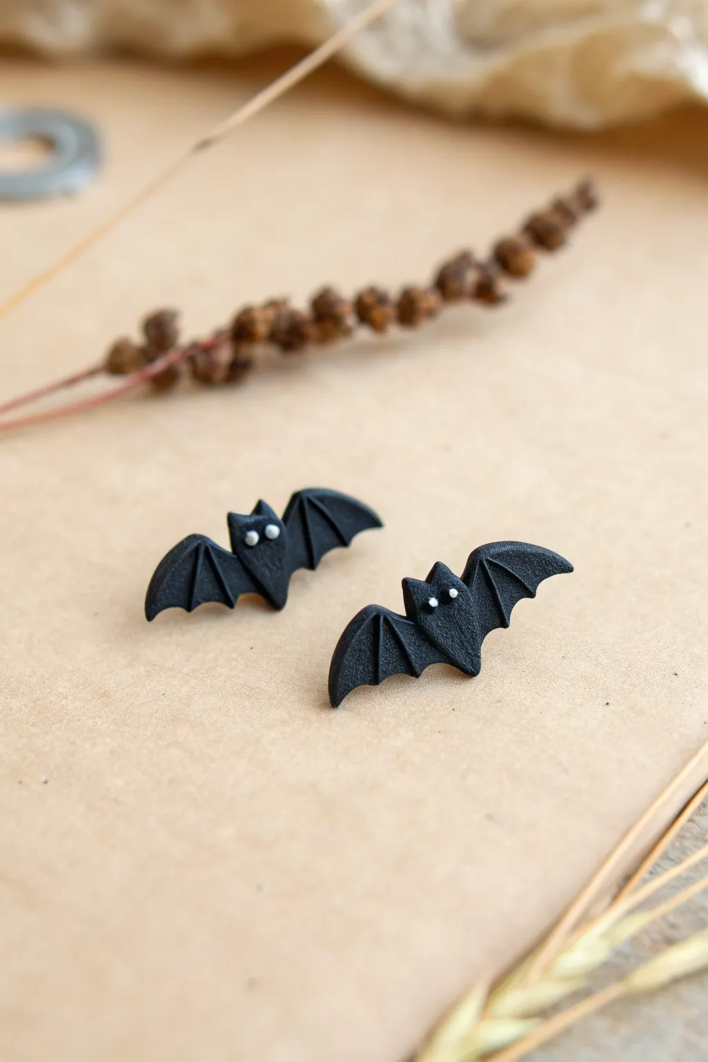 Minimalist black bat stud earrings in polymer clay, styled on linen with subtle autumn warmth