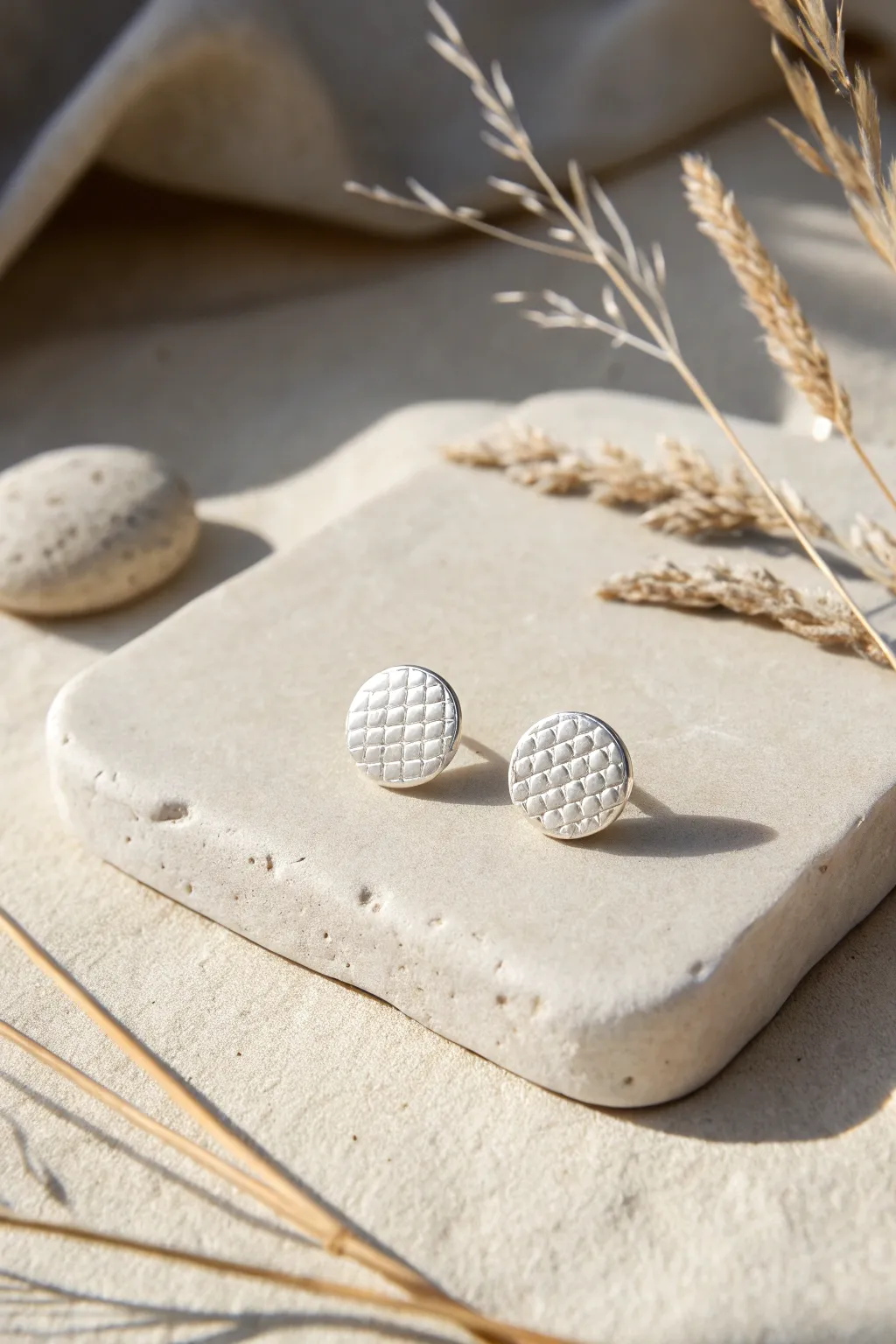 Minimal textured silver disc studs on stone, soft daylight and artisan simplicity.