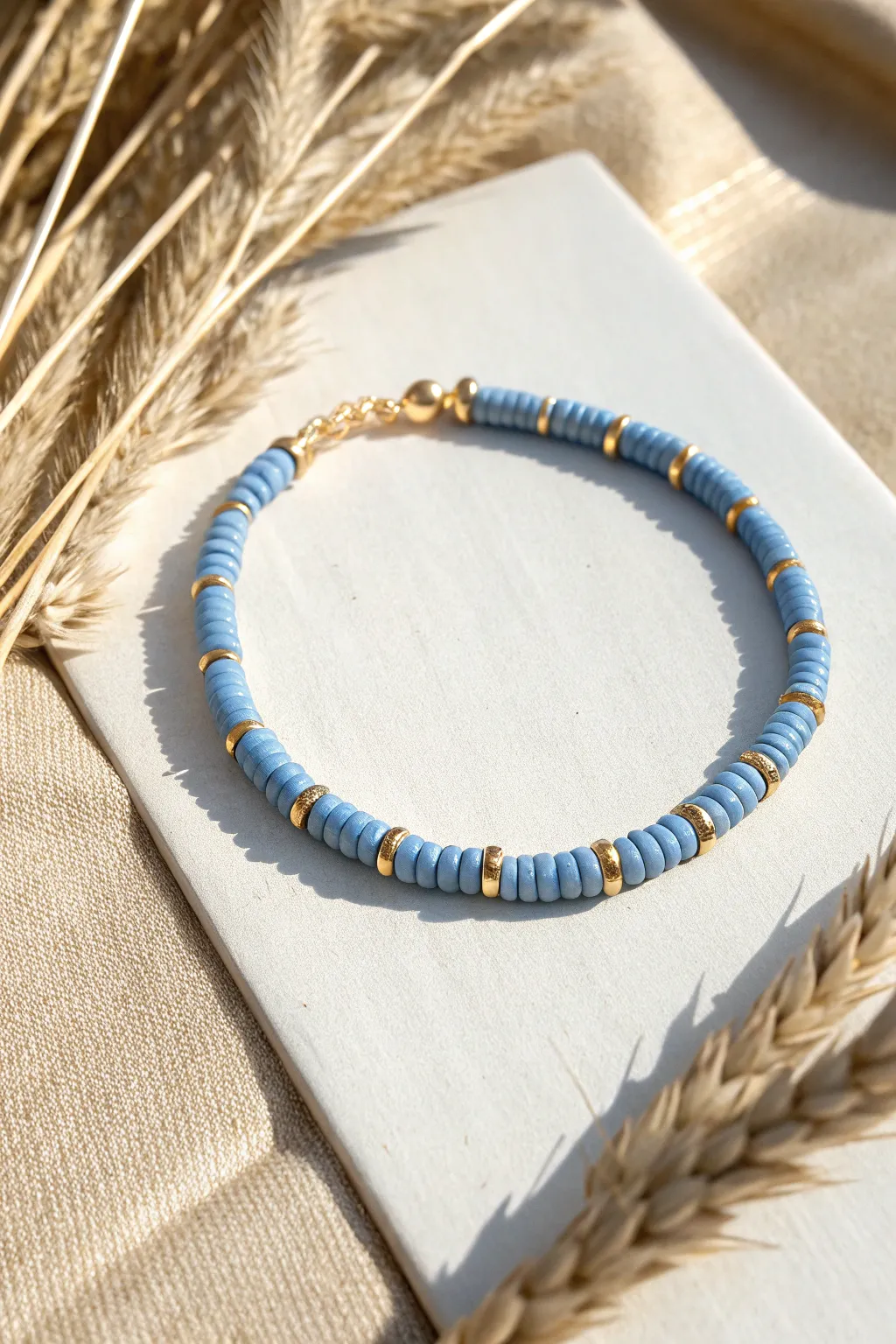Blue heishi bracelet with gold spacers for a crisp preppy pop on a soft beige backdrop.
