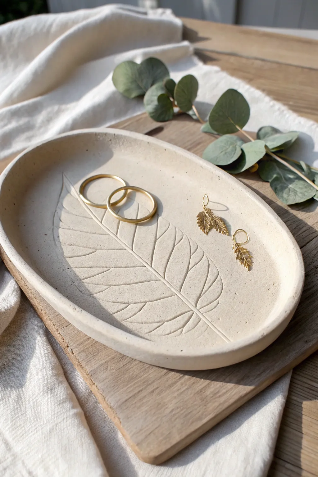 Minimal leaf-imprint air-dry clay tray in soft stone tones, styled with earrings and greenery.