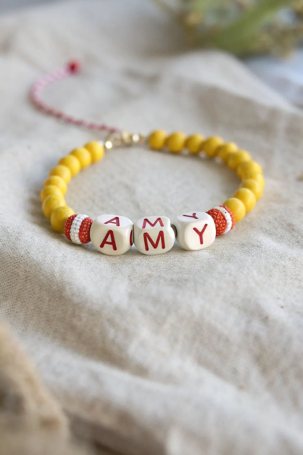 Sunny yellow clay disc bracelet with a personalized name and tiny red accents, game-day sweet.