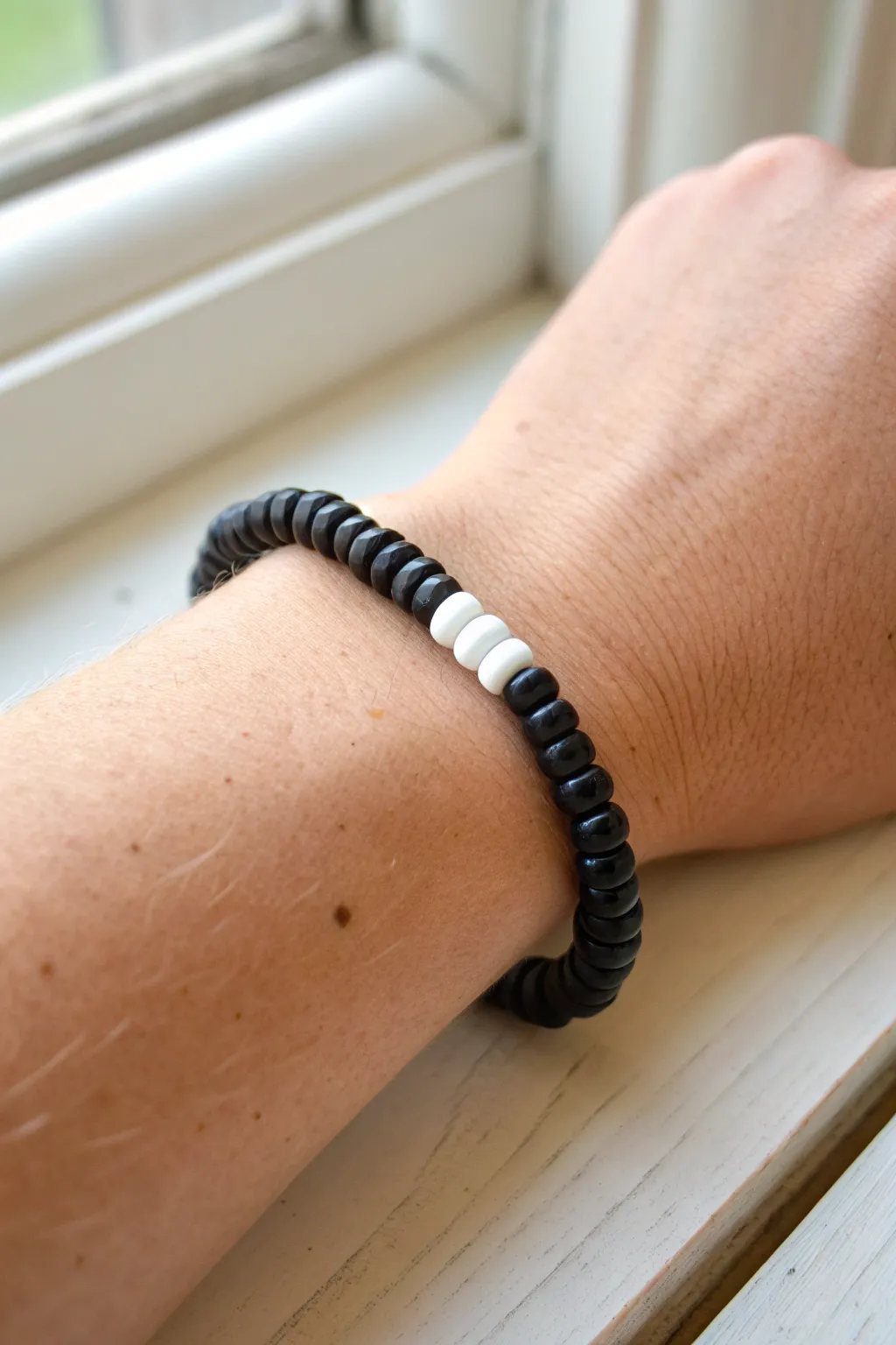 Minimal black heishi bracelet with crisp white center bar, modern contrast with a boho touch.