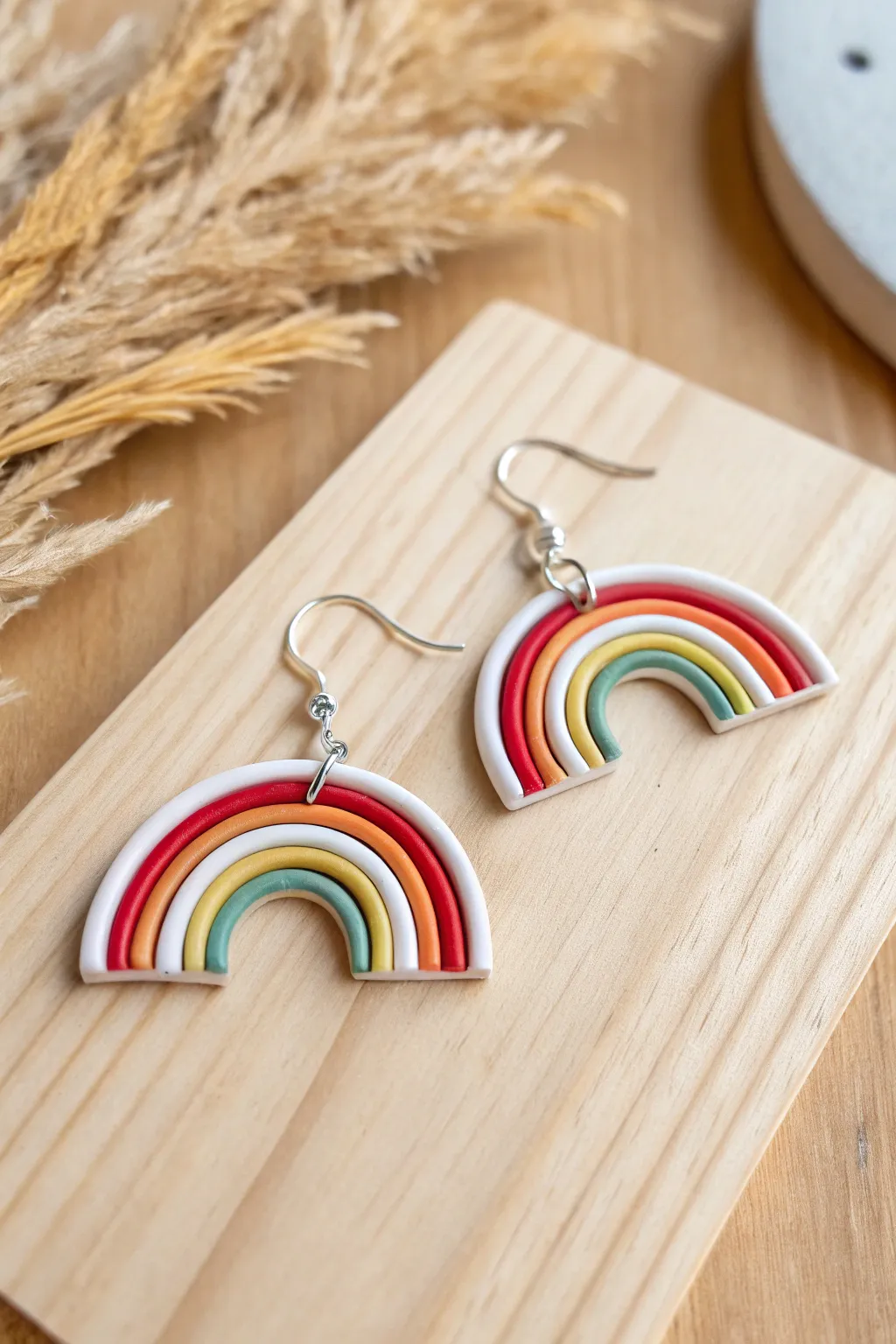 Rainbow arch hoop earrings in bold clay stripes, styled on warm wood with a muted pair behind.