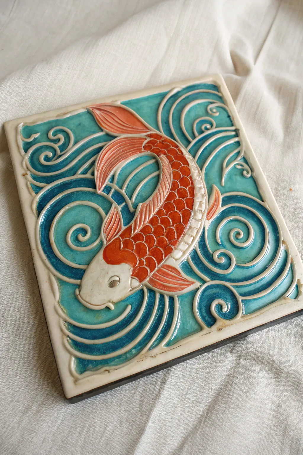Handmade koi relief tile with carved ripples, bold color contrast, minimalist boho vibe.