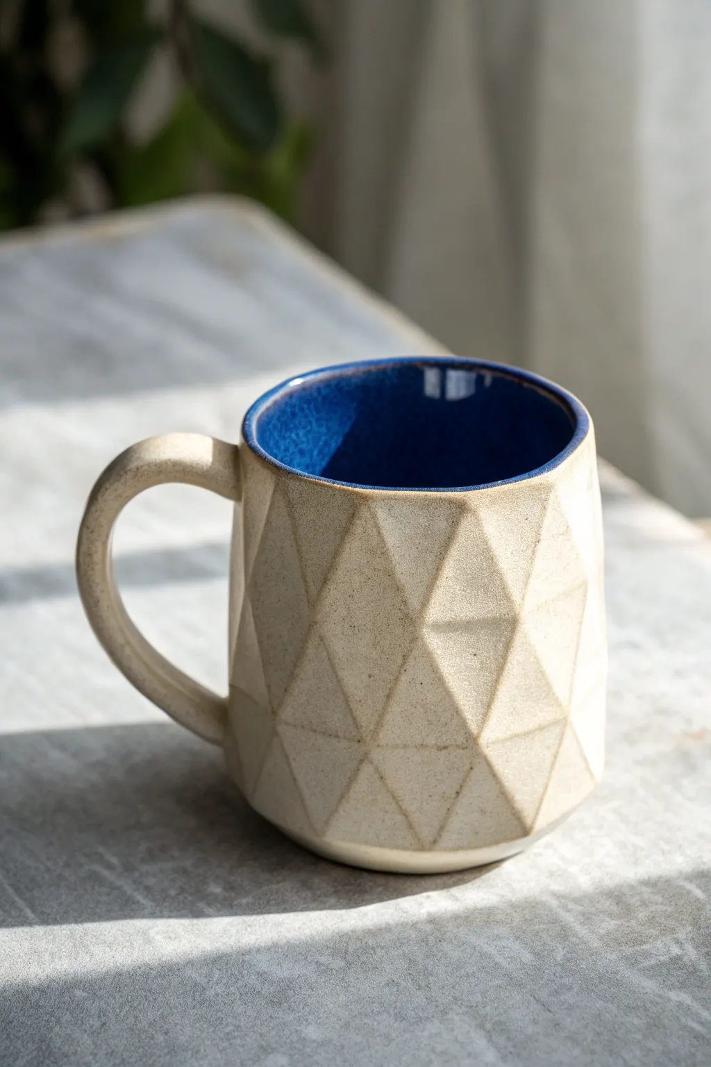 Faceted geometric mug with matte ivory sides and cobalt interior, minimal yet boldly modern.