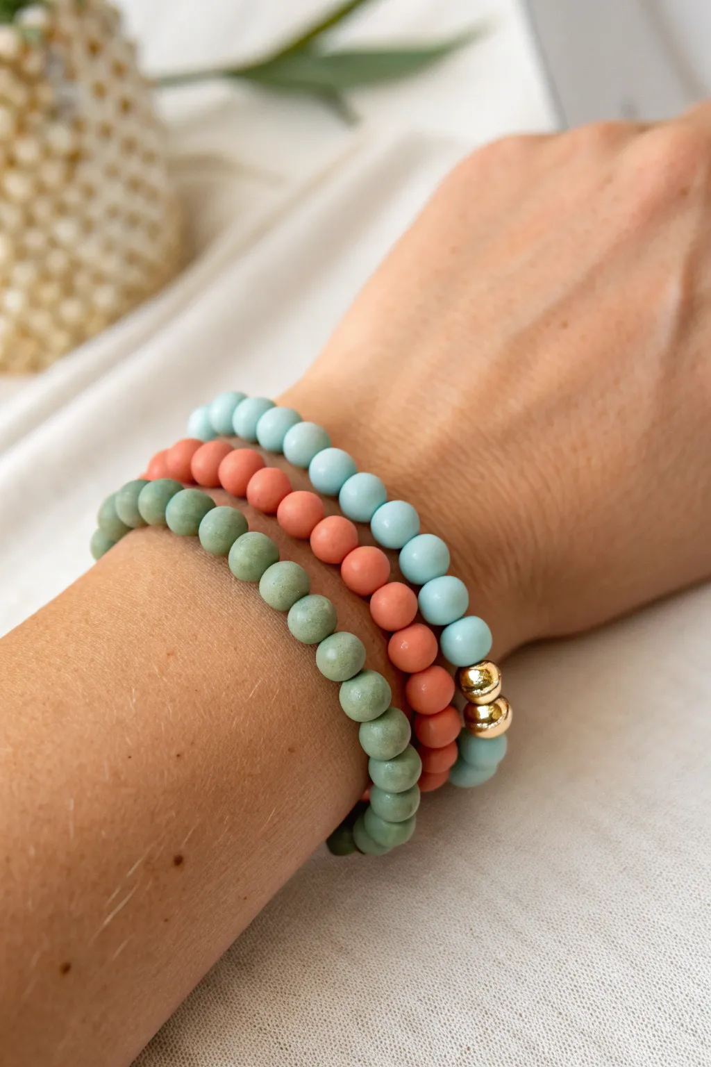 Monochrome clay bead stacks in coral, sage, and sky blue with sleek gold dividers