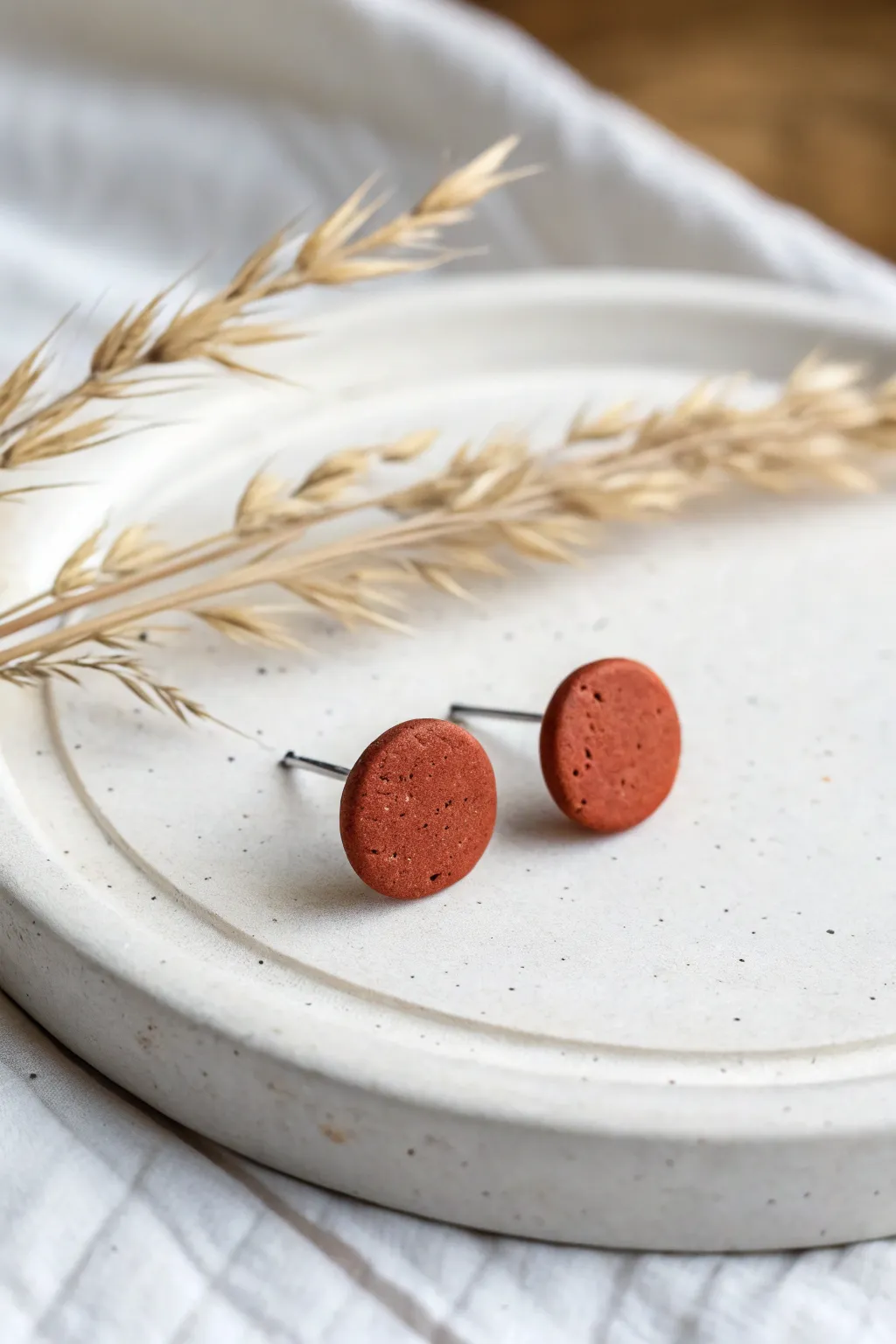 Minimal textured circle studs in oven-bake clay, bold terracotta on clean white ceramic.