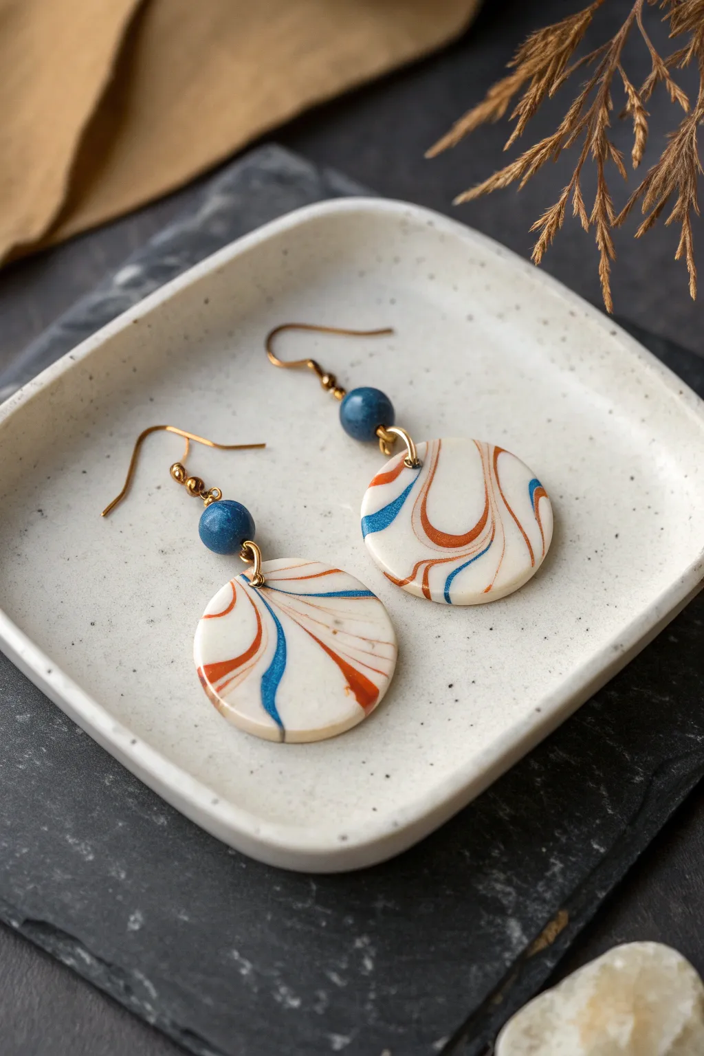Marbled polymer clay dangle earrings with creamy swirls, styled on a stone tray in soft light.