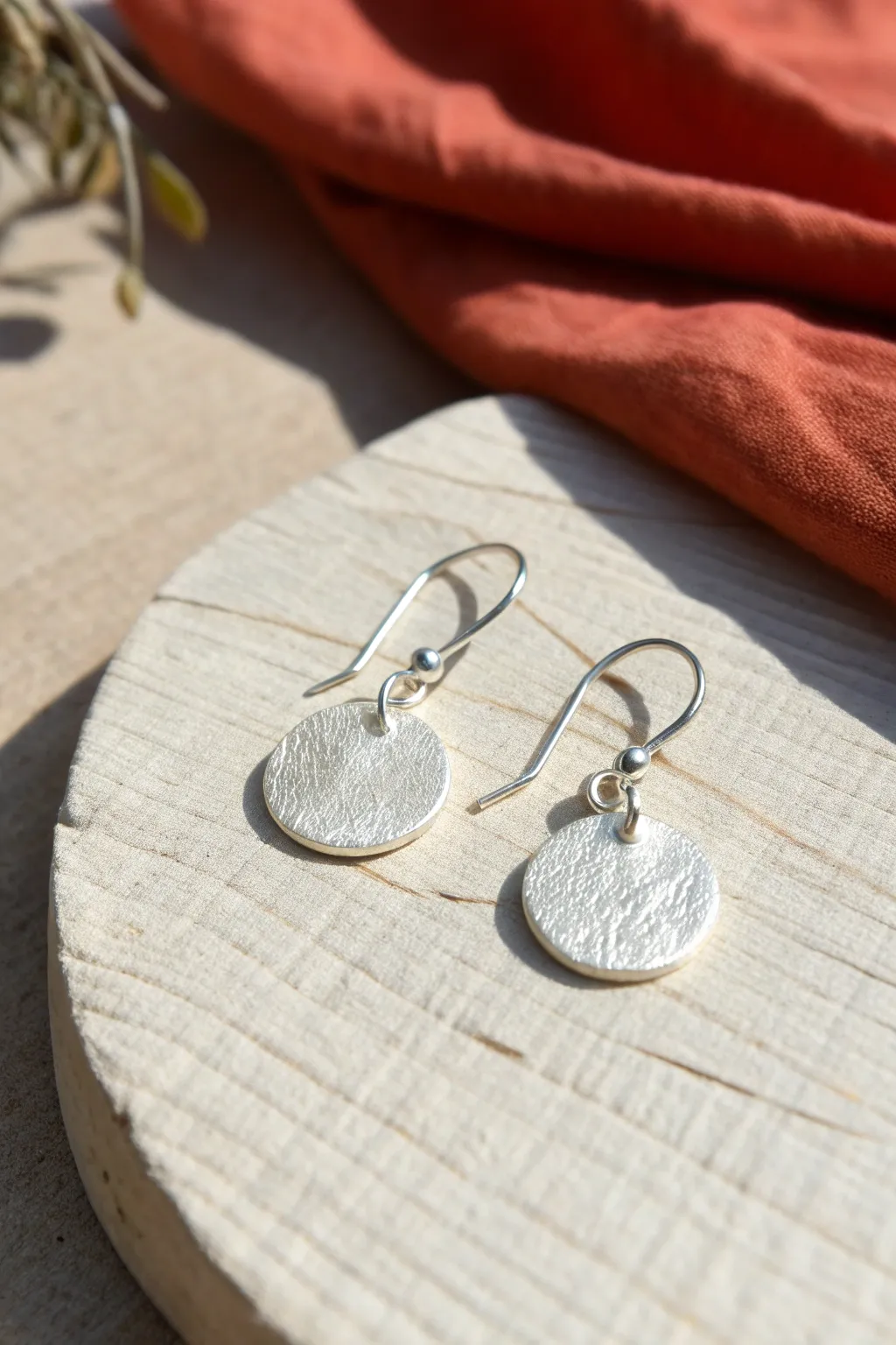 Simple silver clay dangle disc earrings on linen, minimalist Scandinavian style with boho warmth.