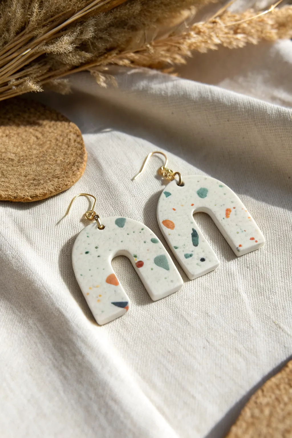 Terrazzo-speckled air-dry clay earrings on linen for an easy, modern boho jewelry DIY.