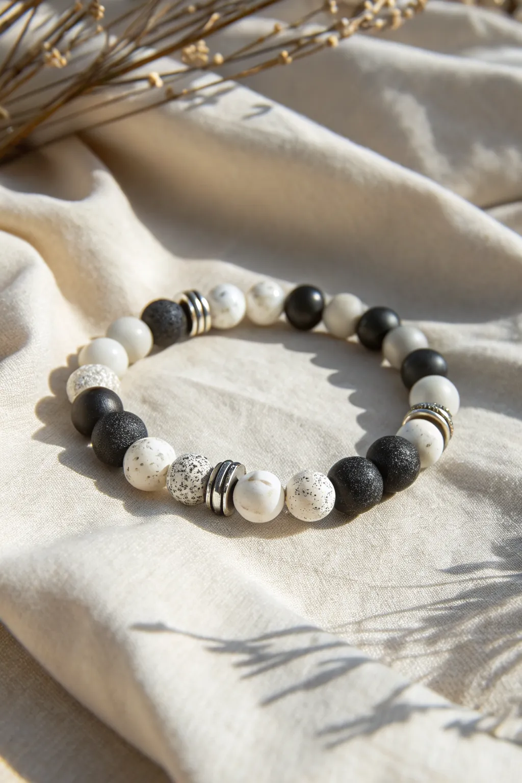 Crisp black-and-white clay bead bracelet with silver spacers on textured cream linen.