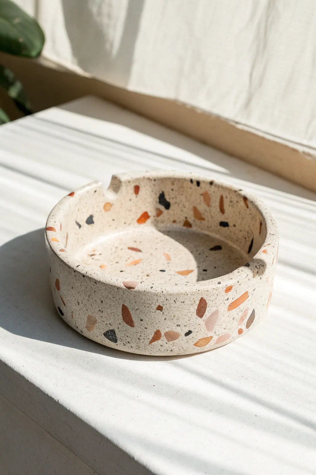Terrazzo-speckled clay ashtray with clean notches, minimalist lines, and soft natural light.