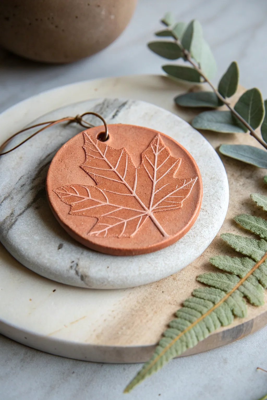 Leaf-print clay medallion with crisp veins, styled simply on linen with fresh greenery nearby.
