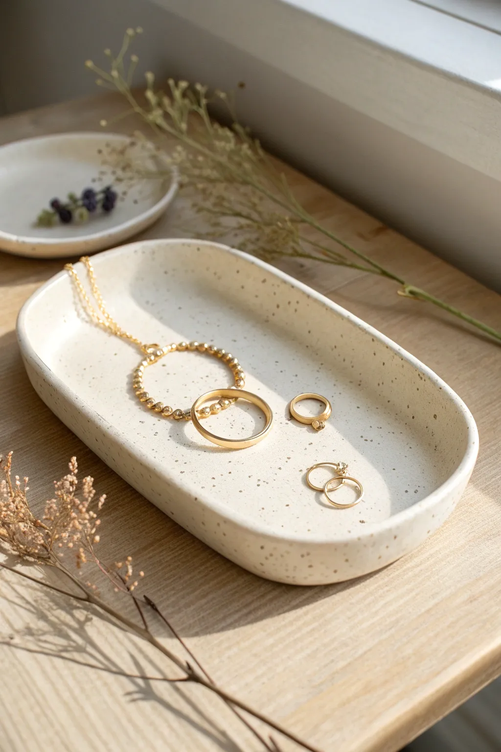 Cream speckled stoneware-look tray styled simply with gold jewelry and a dried stem